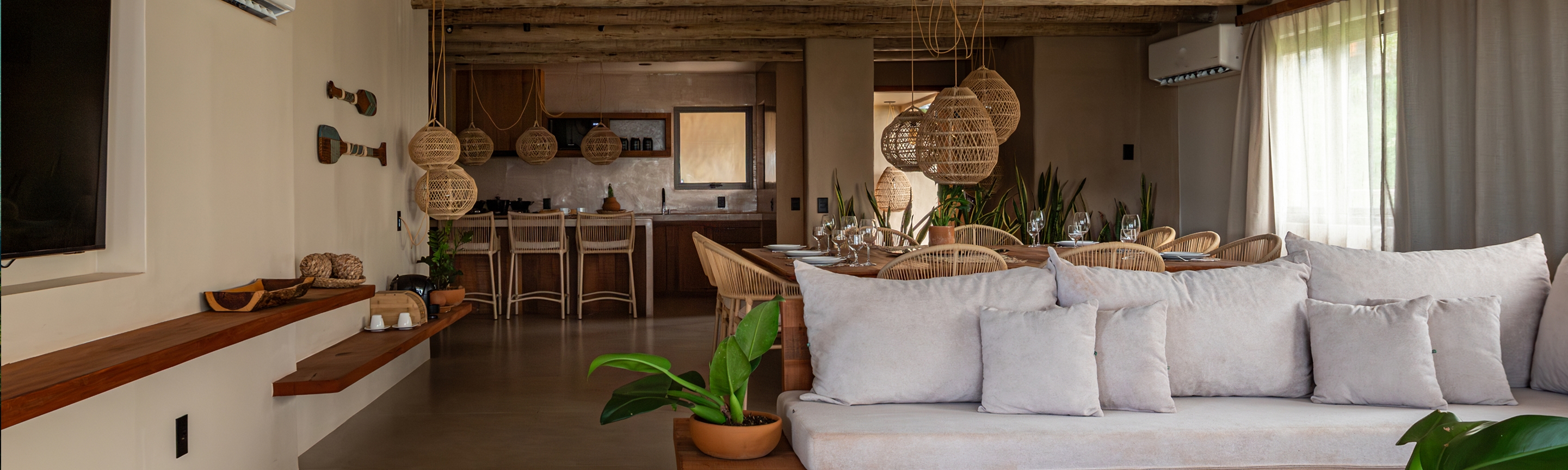 Sala de estar com sofá de almofadas cinza, planta em primeiro plano e luminárias de palha ao fundo