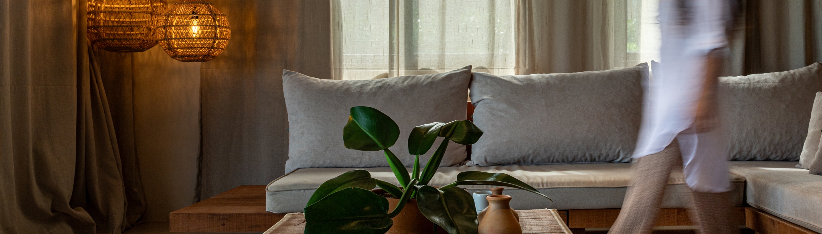 Living room with a grey cushioned sofa, a plant in the foreground and woven pendant lamps in the background